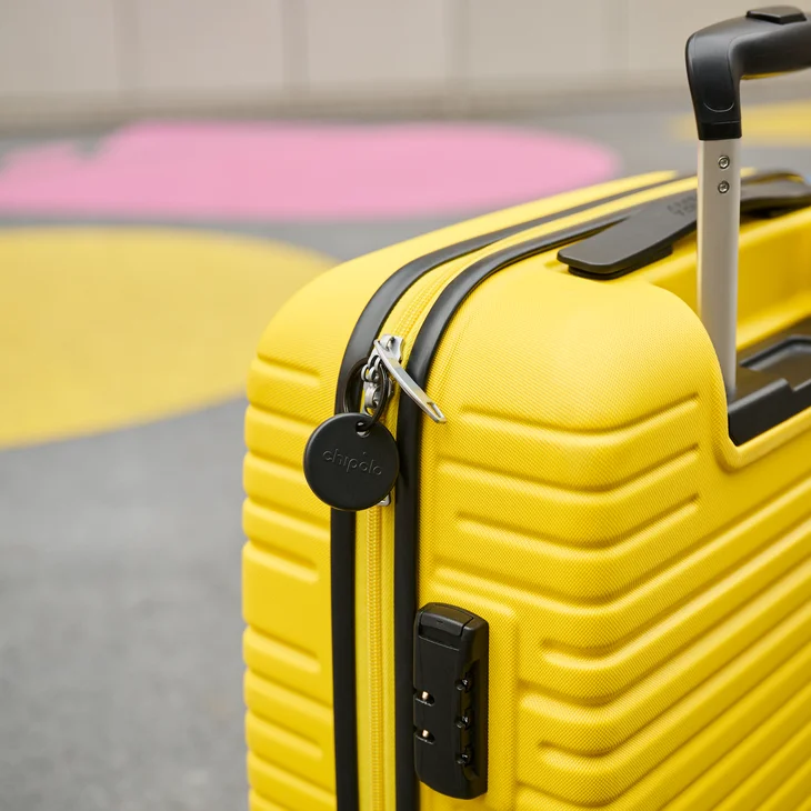 Black Chipolo tracker attached to a yellow suitcase